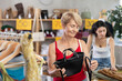 © JackF - Elderly woman in a red top stands in a clothing store and chooses a stylish handbag made of quality material, she carefully looks at it from all sides before buying