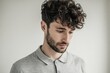 © Tanatchaporn - Young man with curly hair and beard wearing a light gray shirt looking down.