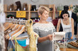 © JackF - Mature woman stands in a store in the sale area of clothes and accessories and carefully chooses a fashionable handbag