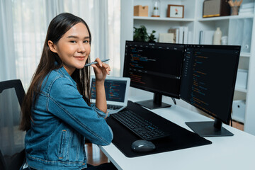 Young Asian in IT developer looking at camera to present with online information on pc with coding program data application, wearing jeans shirt. surround by safety analysis two screens. Stratagem.