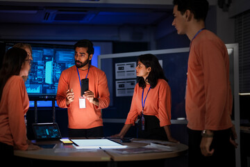 A diverse team of app developers and product designers collaborates on a new mobile device. They are brainstorming ideas for the phone's software and hardware features.