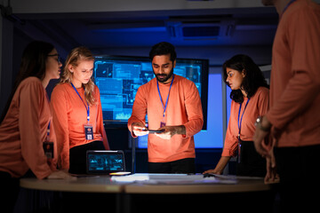 A diverse team of app developers and product designers collaborates on a new mobile device. They are brainstorming ideas for the phone's software and hardware features.