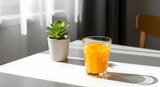 A glass of fresh orange juice sits on a white table beside a small potted succulent in a sunny, minimalist setting.