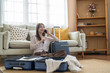 © Art_Photo - Asian woman traveler talking with smartphone and packing clothes in suitcases for travel at home, connected traveler, modern lifestyle, planning holiday travel, content creator and travel blogger