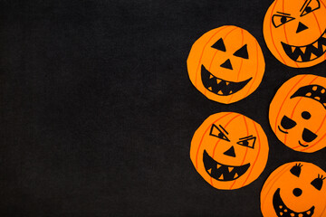 Wall Mural - Orange scary smiling pumpkin faces on dark black table background. Closeup. Creating Halloween decoration. Flat lay. Little child handcraft. Top down view.
