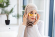 © sofiko14 - Young Muslim woman in beige hijab applying gold hydrogel eye patches for skincare in modern indoor environment. Promoting self-care and healthy lifestyle concept, model demonstrates beauty.
