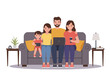 © FRIDA STORE - Family of four seated on a gray sofa using tech devices in a room