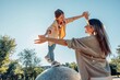 © Westend61 - Mother supporting child balancing outdoors in sunlight