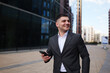 © muse studio - Businessman smiling while using a smartphone outside modern office building