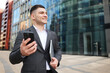 © muse studio - Young man in suit smiling with smartphone and folder in modern city area