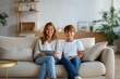 © Iryna - Caucasian siblings relaxing at home with digital devices on sofa