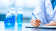 © Allie - Scientist writing notes in laboratory with blue chemical solutions in background