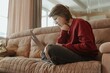 © looking2thesky - A young woman works on her laptop in a cozy living room, capturing the modern freelance lifestyle. Authentic moment of remote work, focus, and digital independence