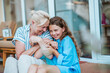 © Halfpoint - Grandmother and granddaughter spending summer together, sitting in front of house.