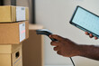 © pressmaster - Black man scanning shipping labels on cardboard boxes with barcode scanner while holding digital tablet, focusing on logistics and inventory management in warehouse setting
