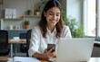 © Brandon - Young hispanic business female manager using laptop, cell phone mobile gadget for working chat. Smiling Latin or Indian woman holding smartphone sitting in office for e commerce shopping or studying