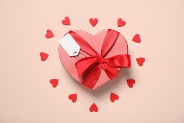 Wall Mural - Gift box with blank tag and decorative hearts on pale pink background, flat lay