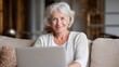 © Johannes - older smiling 60s woman sitting at home on sofa holding laptop senior happy business woman using pc technologies working chatting spending time in social media internet ecommerce no logos no brands a