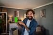 © Migma_Agency - Smiling man presenting smartphone with green screen at home