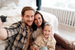 © BullRun - Smiling family hugs tightly for home selfie, child in front glowing with joy, warm intimate moment showing strong connection and modern lifestyle values.