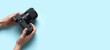© Pixel-Shot - Hands holding modern professional photo camera on blue background with space for text