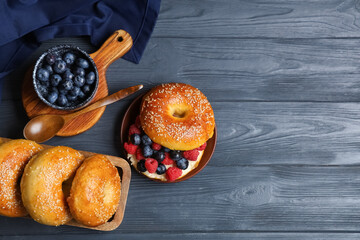 Wall Mural - Board and plate of tasty bagels with berries on blue wooden background