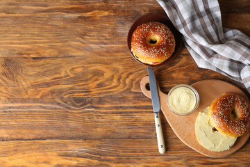 Wall Mural - Board with tasty bagel and glass bowl of butter on wooden background