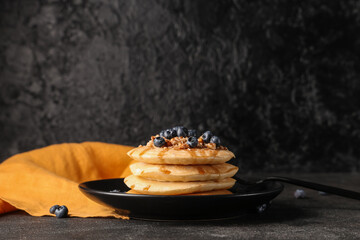 Wall Mural - Plate of sweet pancakes with fresh blueberries and nuts on black background
