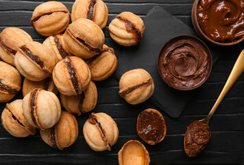 Wall Mural - Sweet walnut shaped cookies with boiled condensed milk on black wooden background, closeup