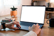 © NAMPIX - A person's hands are visible as they work on a modern laptop with a blank, white screen. The setting is a cozy, wooden desk, suggesting work-from-home