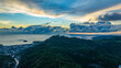 Aerial hyper lapse view of A breathtaking sunset paints the sky in vivid hues of orange and blue over a coastal town, with lush green hills framing the scene. cloud in dramatic sunset over the ocean