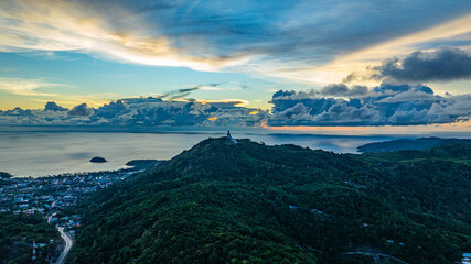 Wall Mural - Aerial hyper lapse view of A breathtaking sunset paints the sky in vivid hues of orange and blue over a coastal town, with lush green hills framing the scene. cloud in dramatic sunset over the ocean