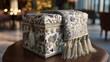 © Pannee - Ornate decorative box with intricate floral embroidery and elegant tassels resting on a wooden table in a stylish interior setting