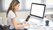 © bongkarn - Asian woman office worker holding phone looking at clipboard and sitting with blank screen computer.