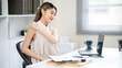 © bongkarn - Smiling asian woman office worker massaging shoulder while looking at laptop at table in office.