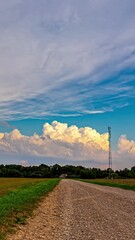 Wall Mural - Layers of cumulus clouds moving along bursting in sky looking scenic over a countryside field.