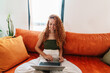 © Westend61 - Smiling woman shopping online sitting cross legged on orange sofa