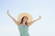 © DG PhotoStock - Woman in dress and wide hat walking at beach shore in morning sun.