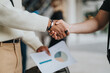 © qunica.com - Close-up of a handshake between two professionals, symbolizing teamwork, agreement, and collaboration. A business chart in the background emphasizes analysis and strategic partnership.