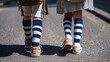 © Katerina Bond - Two schoolchildren walking side by side on a street, seen from behind, wearing matching striped socks and backpacks, suggesting the start of a school day.