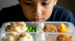 © Tanakorn - Unhappy child looks at school lunch tray reflection on poor cafeteria food quality and waste management. unhealthy meal highlights problems with student nutrition