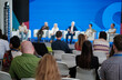© Anton Gvozdikov - Audience watches panel discussion on stage with blue backdrop and seated experts sharing insights