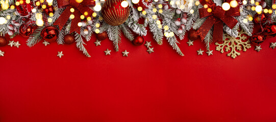 Wall Mural - christmas background with snowy pine branches, red baubles, bells, and festive flowers on a red surf