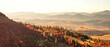 © Denis Rozhnovsky - A breathtaking panoramic view of a mountain range in the Carpathian Mountains during a hazy autumn sunset, with vibrant fall foliage on the hillsides illuminated by the warm, golden light.