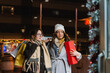© pablo - Two women enjoying festive shopping, carrying bags and a red gift box