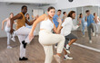 © JackF - Group of cheerful young adult diverse dancers performing dynamic movements with knee up in modern fitness studio