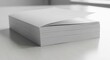 © Djemari - A stack of blank white paper sits on a light-colored surface, with the top sheet slightly lifted, suggesting readiness for use.