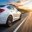 © LuxeLiving - White car speeds on an open highway into the sunset, with rolling mountains in the distance, capturing a sense of freedom and adventure