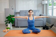 © Pang - A young woman practicing yoga indoors on an exercise mat, using a laptop for online training, symbolizing health, strength, and wellbeing.
