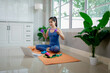 © Pang - A young woman practicing yoga indoors on an exercise mat, using a laptop for online training, symbolizing health, strength, and wellbeing.
